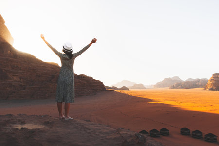Happy joyful woman tourist stand with hands up on cliff barefoot at viewpoint and enjoy holiday vacation in Wadi rum panorama on sunrise. Popular Wadi Rum desert in Jordanの写真素材