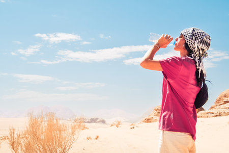 Thirsty desert traveler young caucasian woman with face red of sun burn drinking water. Side view with panorama of hot desertの写真素材