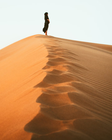 Woman silhouette enjoy sand dunes in desert in sunset blue hour alone. Travel lifestyle and wellness concept. Cinematic wanderlust backgroundの写真素材