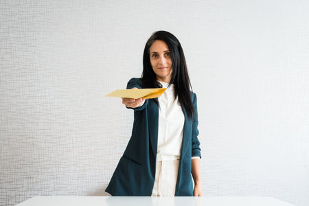 Young caucasian brunette business woman director in office hand show give envelope job contract or agreement, wage slip yellow envelope n hands with smileの写真素材
