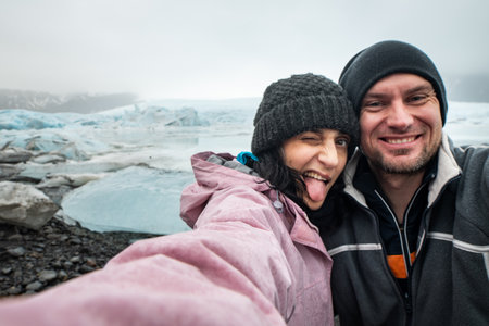 Funny travelous couple taking self portrait photograph on Iceland having fun on travel by Jokulsarlon glacial lagoon / glacier lake. Tourists enjoying beautiful Icelandic nature landscape Vatnajokull.の写真素材