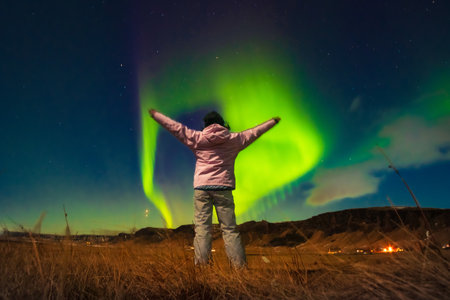 Woman watches the northern lights arms up excited joyful in Iceland. Woman in Icelandic spring night landscape. Iceland travel chasing northern lights conceptの写真素材