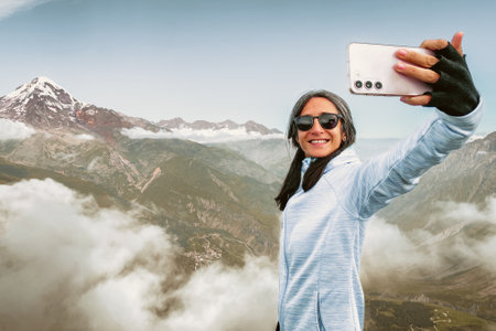 Brunette Young cute woman taking selfie portrait hiking mountains - Happy hiker on the top of the cliff smiling at camera - Travel and hobby conceptの写真素材