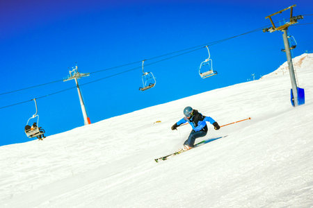 Side view male skier wear blue isolated on piste ski downhill fast motion in Alps. Active winter holidays, skiing downhill in overcast day. Ski rides on the track with swirls of fresh snowの写真素材