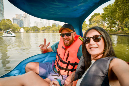 Happy young caucasian couple take selfie look at camera enjoy sport activity on pedal boat in famous public Lumphini park in summer. Bangkok relaxation leisure activitiesの写真素材