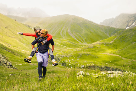 Sporty caucasian couple hikers having fun hiking outdoors do piggyback enjoy holidays - Happy healthy friends laughing together do sports - People outdoors conceptの写真素材