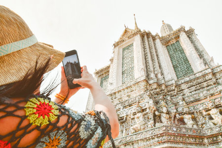 Close up woman tourist taking photo using mobile phone by beautiful Wat Arun temple in Bangkok, Thailand. Famous tourist destination content creator concept post social mediaの写真素材