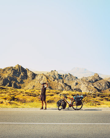 Cinematic travel inspirational panorama traveler cyclist stand on road take smiley self-portrait with mobile phone. Solo travel bicycle touring around the worldの写真素材