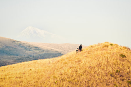 Fit young caucasian male person push bicycle uphill with mountains background outdoors in caucasus mountains. Achievement , inspiration, challenge and determination conceptの写真素材