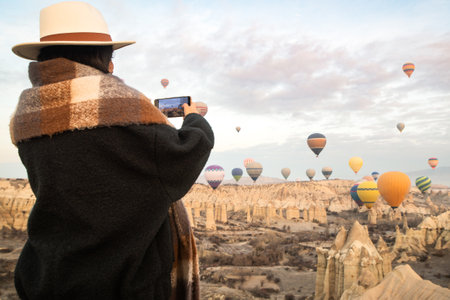 Caucasian woman tourist taking photo of flying hot air balloons take-off viewpoint enjoy sunrise in Cappadocia at holiday - Happy traveler laugh enjoy vacation - People and winter holidays conceptの写真素材