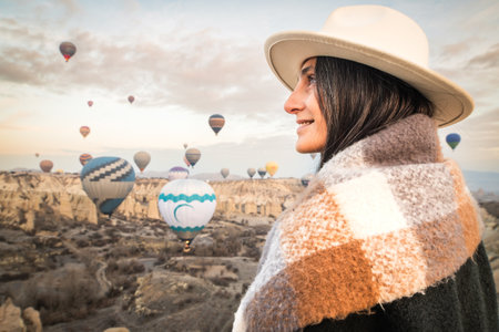 Close up caucasian woman tourist watching hot air balloons take-off from viewpoint smile to camera in Cappadocia at holiday - Happy traveler laugh enjoy vacation visit Cappadocia in Turkeyの写真素材