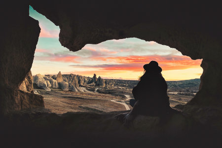 Silhouette woman sit cave on geological formations of Cappadocia watch wonderful sunset sky with fairy chimney panorama. Goreme travel destination. Turkey holiday destination. Unesco world heritageの写真素材