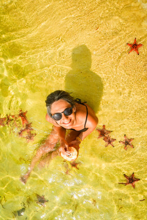 Young happy woman tourist visit pose with starfish in famous tropical Koh Rong island, Cambodia....