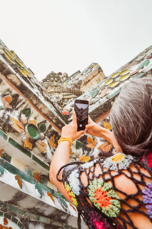 Close up woman tourist taking photo using mobile phone by beautiful Wat Arun temple in Bangkok, Thailand. Famous tourist destination content creator concept post social mediaの写真素材