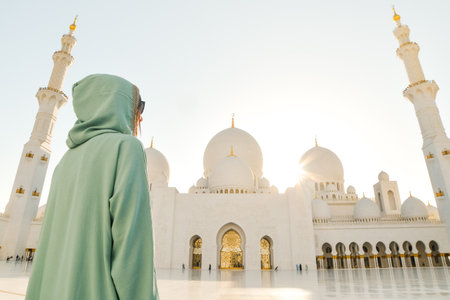 a tourist girl in a muslim dress Abaya pose travel photo while travels through the Great Mosque of Sheikh Zayed in Abu Dhabiの写真素材