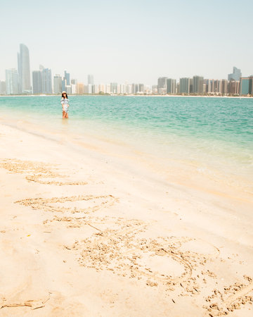 Happy young female tourist on viewpoint in hot day visiting Abu dhabi, UAE - Traveller girl taking portrait in front of capital skyline background. Urban middle east city life travel attractionsの写真素材
