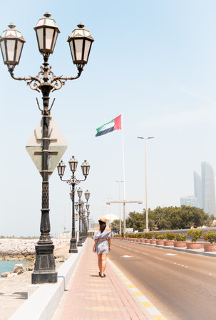 A woman tourist walks along sidewalk with the UAE flag in the background, blending everyday life with a sense of culture, identity, and national prideの写真素材