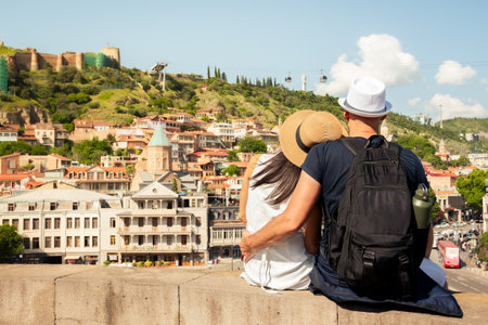Romantic Couple sits close on viewpoint enjoying cityscape view of Old Tbilisi with Narikala...