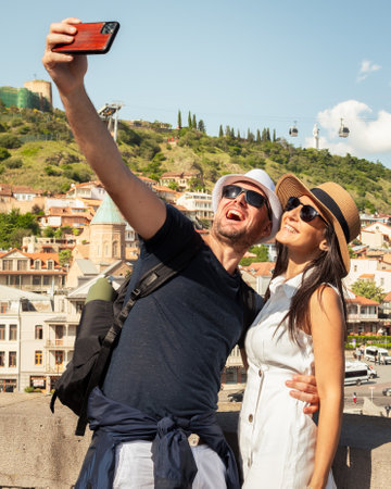Happy couple takes selfie in front of Tbilisiâ€™s Old Town skyline with Narikala Fortress and...