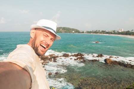 Young excited caucasian male tourist traveler doing selfie overlooking the tropical ocean in south east asia. Adventure, vacation, wanderlust, internet, technology, social media face postの写真素材