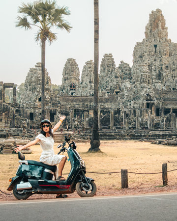 Happy young caucasian tourist driver with electric scooter stand by famous Angkor wat historical site temples - Angkor Thom. Travel explore south-east asia with rented scooter conceptの写真素材