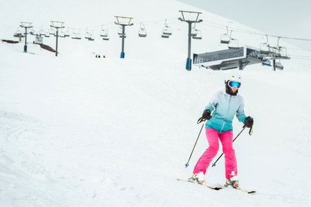 Woman skier in bright clothes skiing slowly on beginner slope with ski lift and station in Gudauri ski resort, Georgia Caucasus mountainsの写真素材