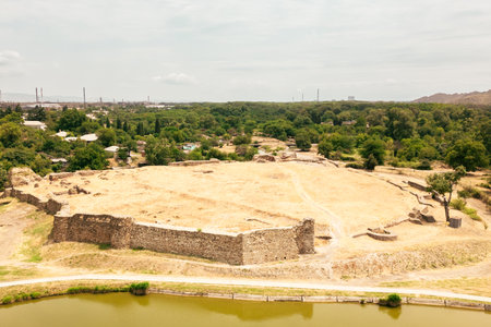 Aerial zoom in view of ancient Rustavi Fortress ruins near lake surrounded by greenery and urban landscape in Georgia symbolizing history heritage and cultural tourismの写真素材