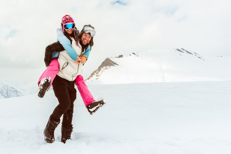 Joyful young loving couple walk piggyback smiling in deep snow share romantic bonding on snowy mountain, love, happiness, freedom, playful relationship, romantic adventure, carefree winter escapeの写真素材