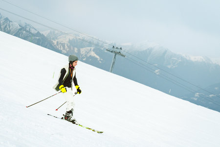 Teenage skier on snowy beginner slope with ski lift chairs passing above at Gudauri ski resort in Caucasus mountains Georgiaの写真素材