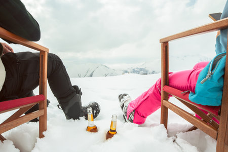 Couple relax sit on chairs in snowy ski resort with beer bottle, concept of leisure, winter holiday, relaxation, carefree lifestyle, freedom, cozy outdoor relaxation momentの写真素材