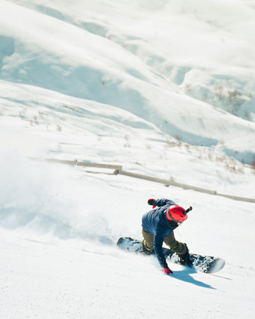 Side view male snowboarder wear blue outfit on piste ski downhill fast motion in Alps. Active winter holidays, skiing downhill in overcast day. Ski rides on the track with swirls of fresh snowの写真素材