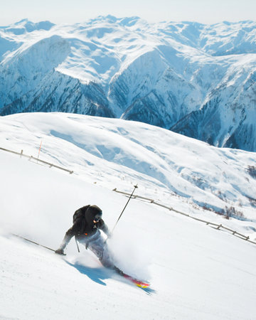 Professional caucasian skier at full speed ski downhill fast motion spray on fresh snow do carving in ski resort while training for competition in ski resort with sunny blue mountains backgroundの写真素材
