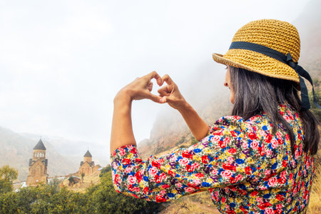 A happy woman show form heart with hands admires loves view of the famous Armenian monastery of...