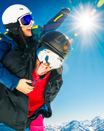 Happy young caucasian skiers couple in love having fun together playing in mountains piggybacking at...