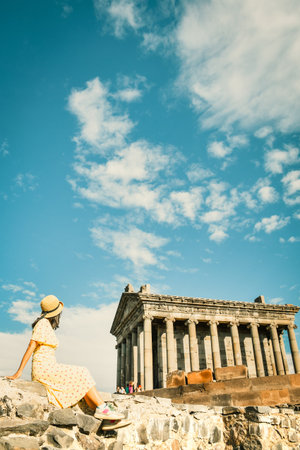 Happy tourist blogger sit enjoy views by famous roman The Garni Temple - classical colonnaded...