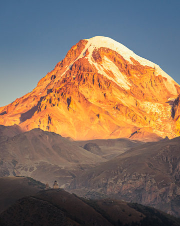 Dramatic sunrise over snowcapped Mount Kazbek with Gergeti Trinity Church in the foreground near...