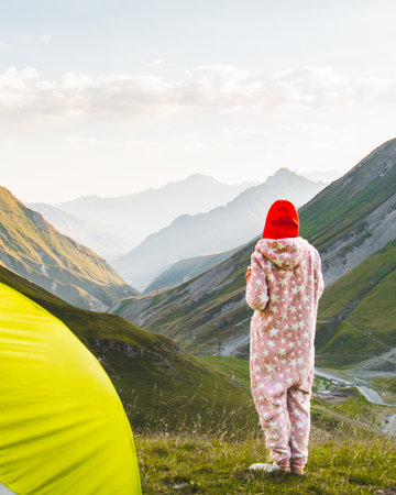 Person in warm pajamas near tent overlooking scenic Kazbegi mountain valley in Georgia at sunriseの写真素材