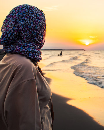 Iranian woman in headscarf watching sunset over Caspian Sea shoreline in northern Iran, symbol of travel, reflection, and golden hour nature beautyの写真素材