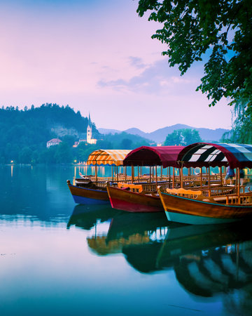 Colorful wooden boats docked on Lake Bled with scenic view of Bled Island church and mountains at dusk in Sloveniaの写真素材