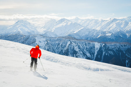 Male adult skier in red jacket go freestyle off piste carving turns to fresh powder mountainside in snowy mountain resort during sunny winter day adventure in alpine high mountainsの写真素材