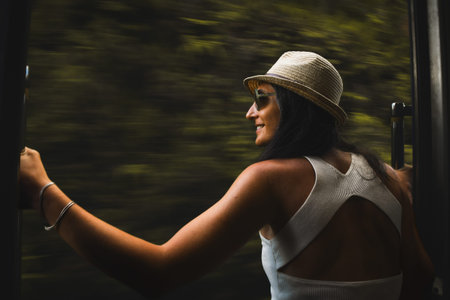 Happy passenger woman tourist stand by doorstep enjoy popular train ride journey Kandy to Ella and admire Sri lanka lush jungle landscapes. Embrace freedom, curiosity, wonder and serenity conceptの写真素材