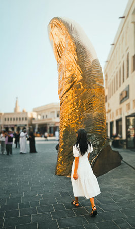 Doha, Qatar - 22nd january, 2026: Woman walking toward monumental thumb sculpture in Katara Cultural Village Doha showcasing contemporary public art urban culture travel landmark experienceの写真素材