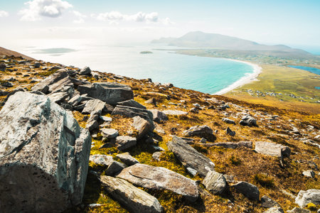 Scenic view from hillside rocks over Achill Island coastline in Ireland with turquoise Atlantic waters, sandy beach, and rugged mountains in backgroundの写真素材