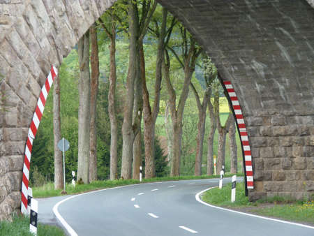   Arch bridge over an empty country road with a view of trees and fieldsの写真素材