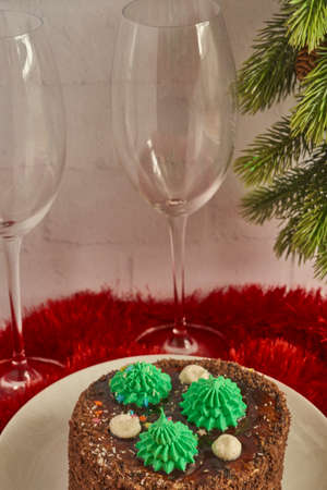 Ð¡hocolate cake decorated with Christmas trees, wine glasses and a fir branch on a red background