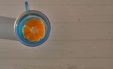 Tangerine is cut in half in an blue cup with water, on a light backgroundの写真素材