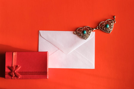 Concept for valentine's day. A envelope with Valentine card, chain of two metal hearts and a gift on a red background with space for text or logo.の写真素材