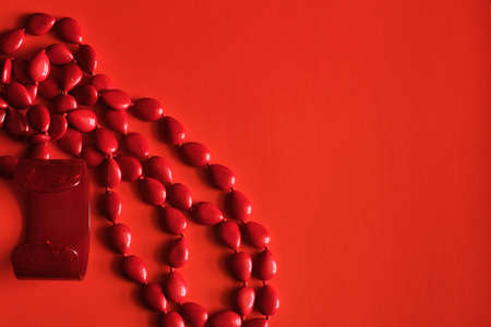 Red beads and a pearl bracelet on a red background with space for text or logo.の写真素材