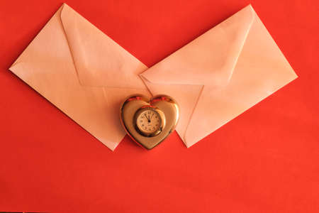 Concept for valentine's day. Two envelopes with Valentines and a heart-shaped clock on a red backgroundの写真素材