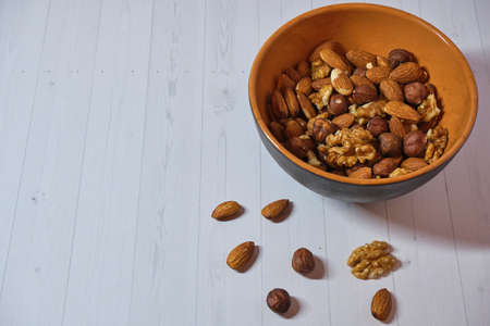 brown clay bowl with nuts: walnuts, almonds and hazelnuts on a light backgroundの写真素材